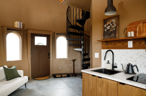 Cozy interior of a small home featuring a spiral staircase, kitchen area, and a door with arched windows.